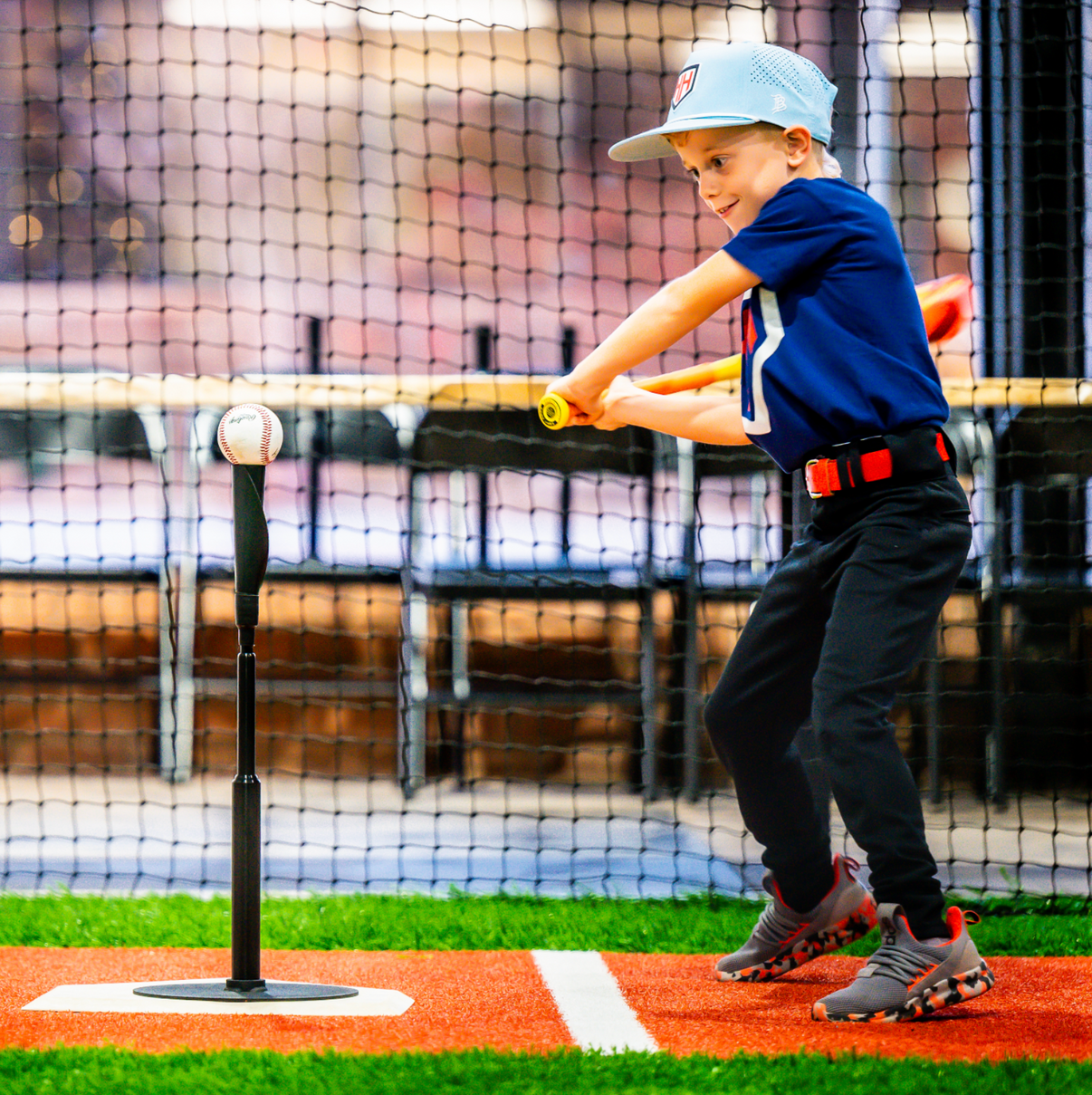Young baseball player hitting baseball off of tee in batting cages