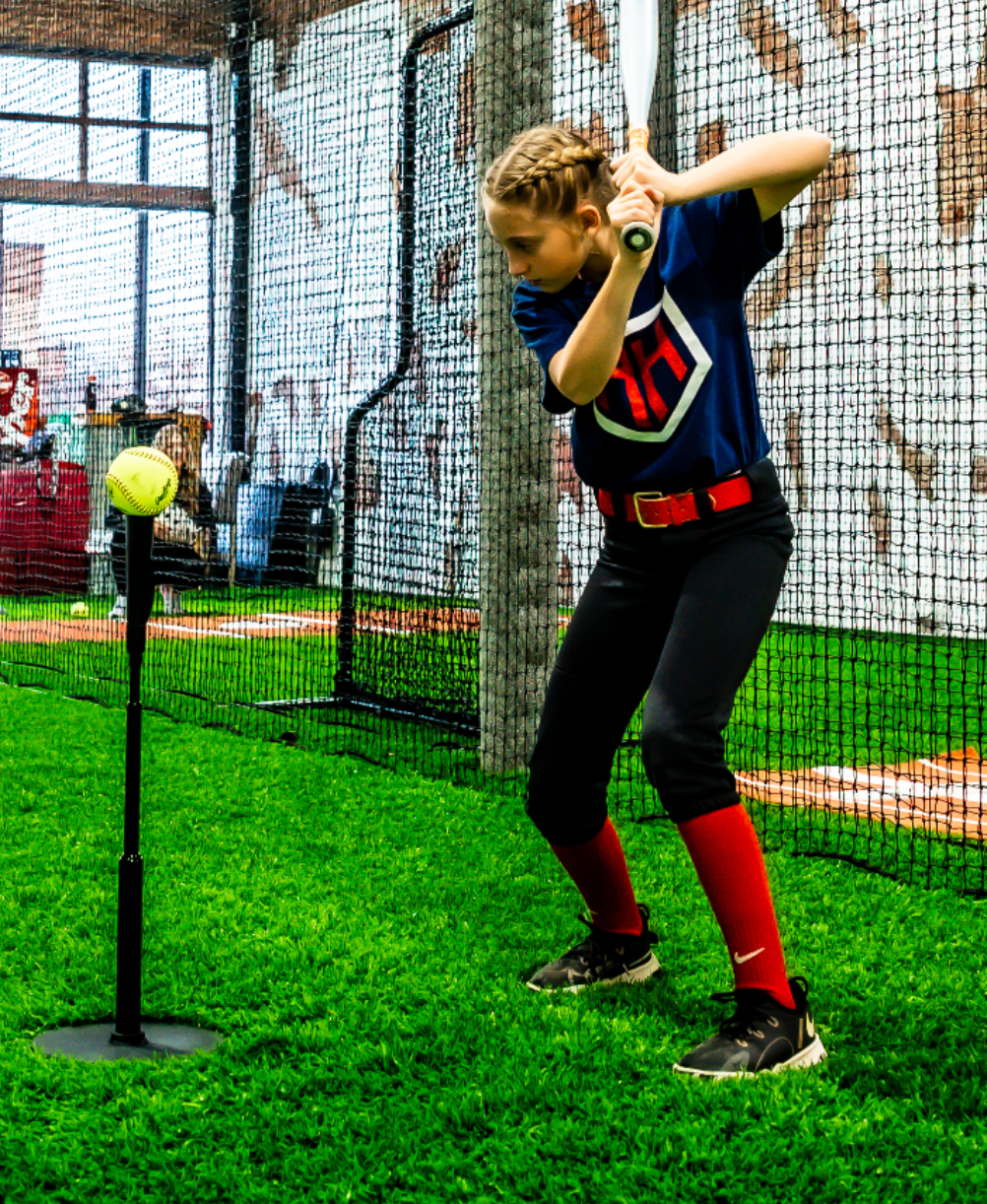 Young softball player hitting softball off of Home Run Hero tee in batting cage