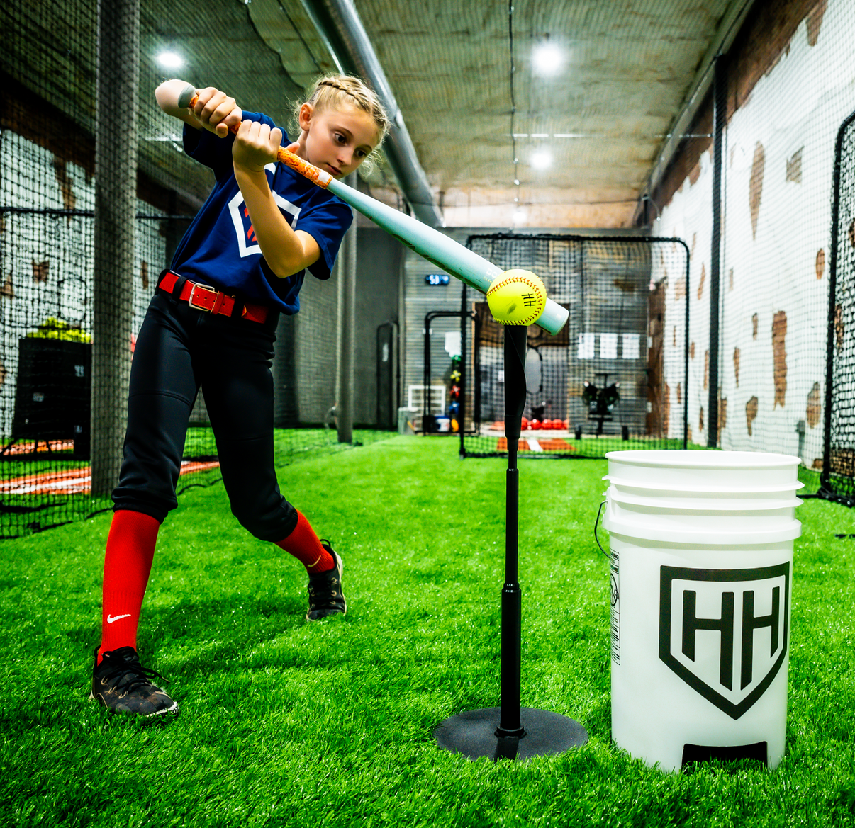 Softball player hitting softball off of Home Run Hero tee in batting cage