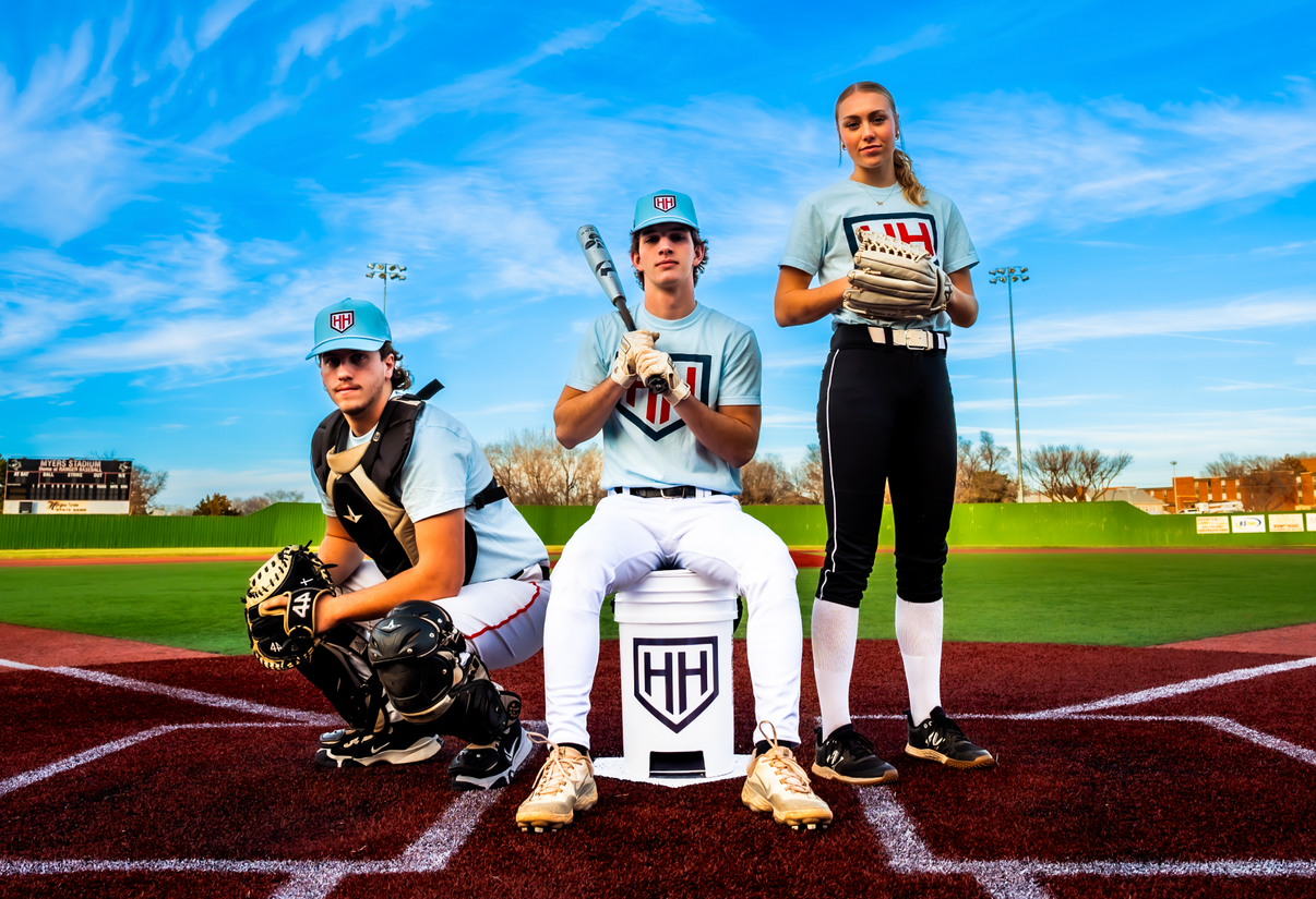 Home Run Hero baseball and softball players sitting on bucket and crouching in catcher gear and standing with mitt on by the home plate of stadium