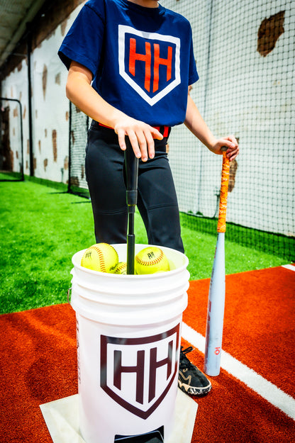 Young softball player pushing down tee in Home Run Hero ball bucket