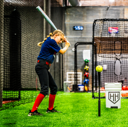 Young softball player hitting softball off of Home Run Hero tee in batting cage